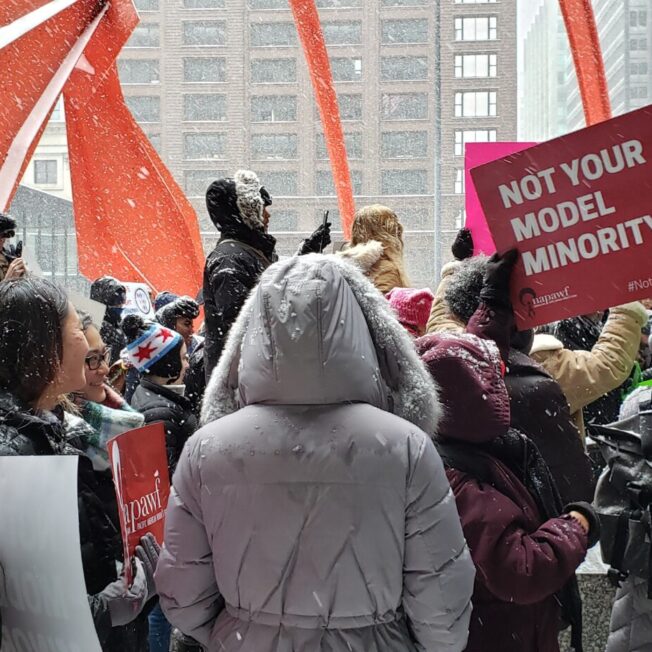 A crowd in Chicago holds signs that say Not Your Model Minority