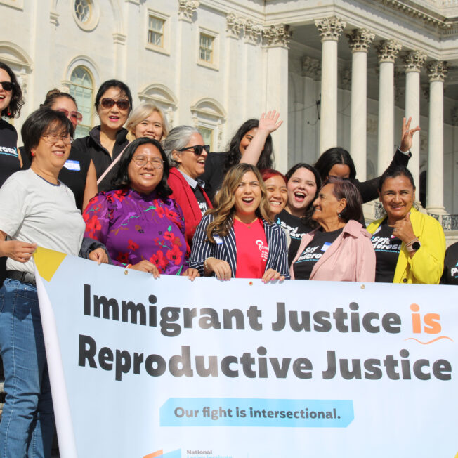 A group of Asian American and Latinx activists smile while holding a sign that says Immigrant Justice is Reproductive Justice