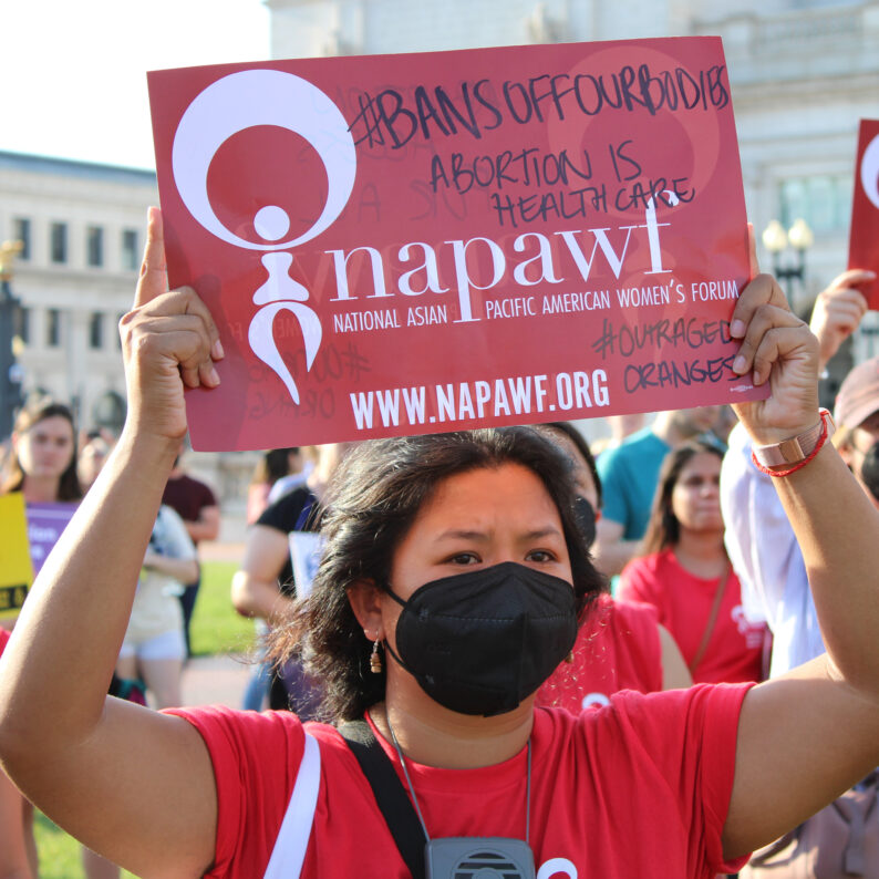 A young Cambodian American woman holds a sign that says Bans off our bodies. Abortion is health care!