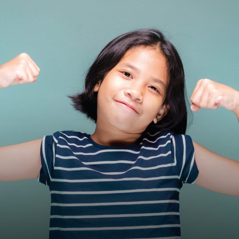 An Asian girl triumphantly lifts both her arms.