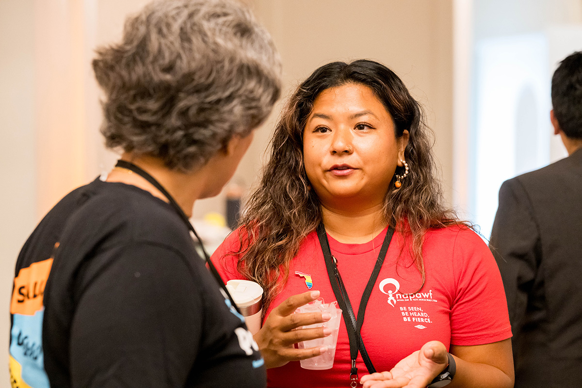 A person in a NAPAWF shirt with a rainbow florida pin talks to another person in a Latina Institute shirt